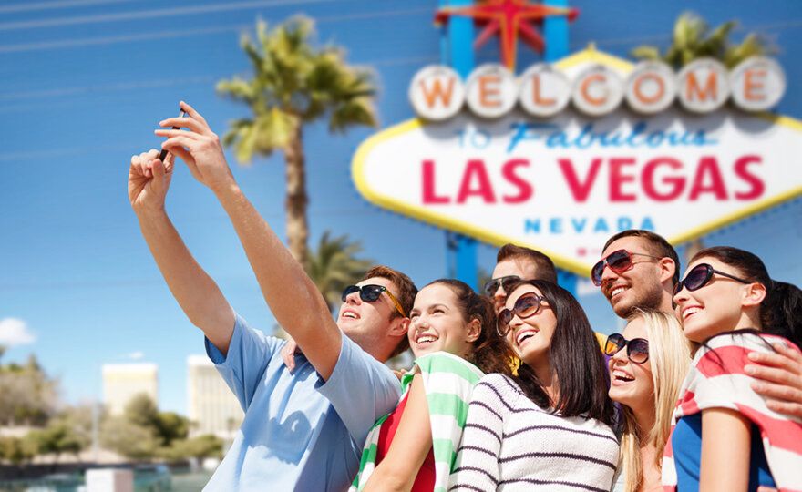 travel and tourism concept - group of happy friends taking selfie by cell phone over welcome to fabulous las vegas sign background